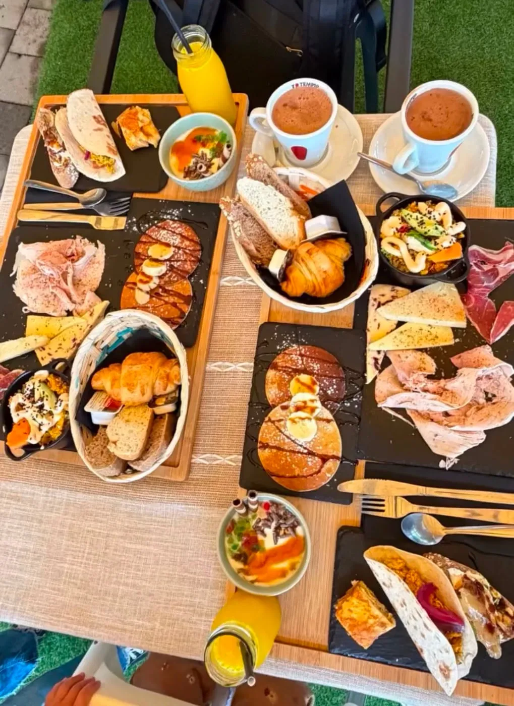 Mesa de brunch para dos, con tortitas, zumos, panes, croissants y bol de quinoa