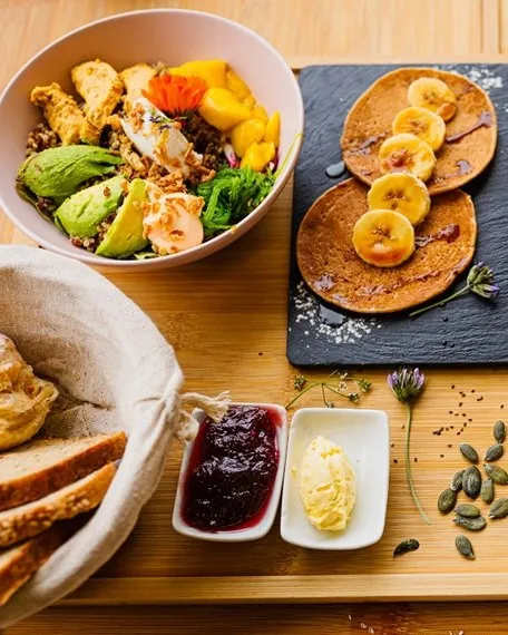 Brunch con bol de poke, tortitas con plátano y cesta de panes
