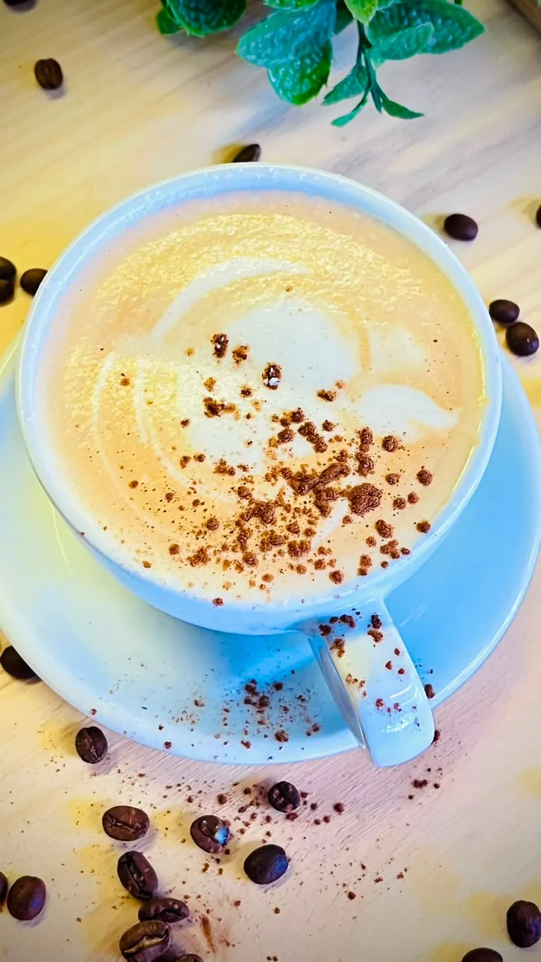 Cappuccino con cacao espolvoreado, entre granos de café