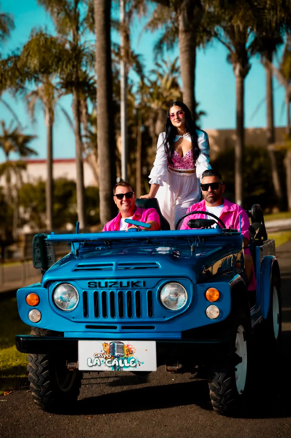 Los tres integrantes de Grupo La Calle sobre un jeep azul, entre palmeras
